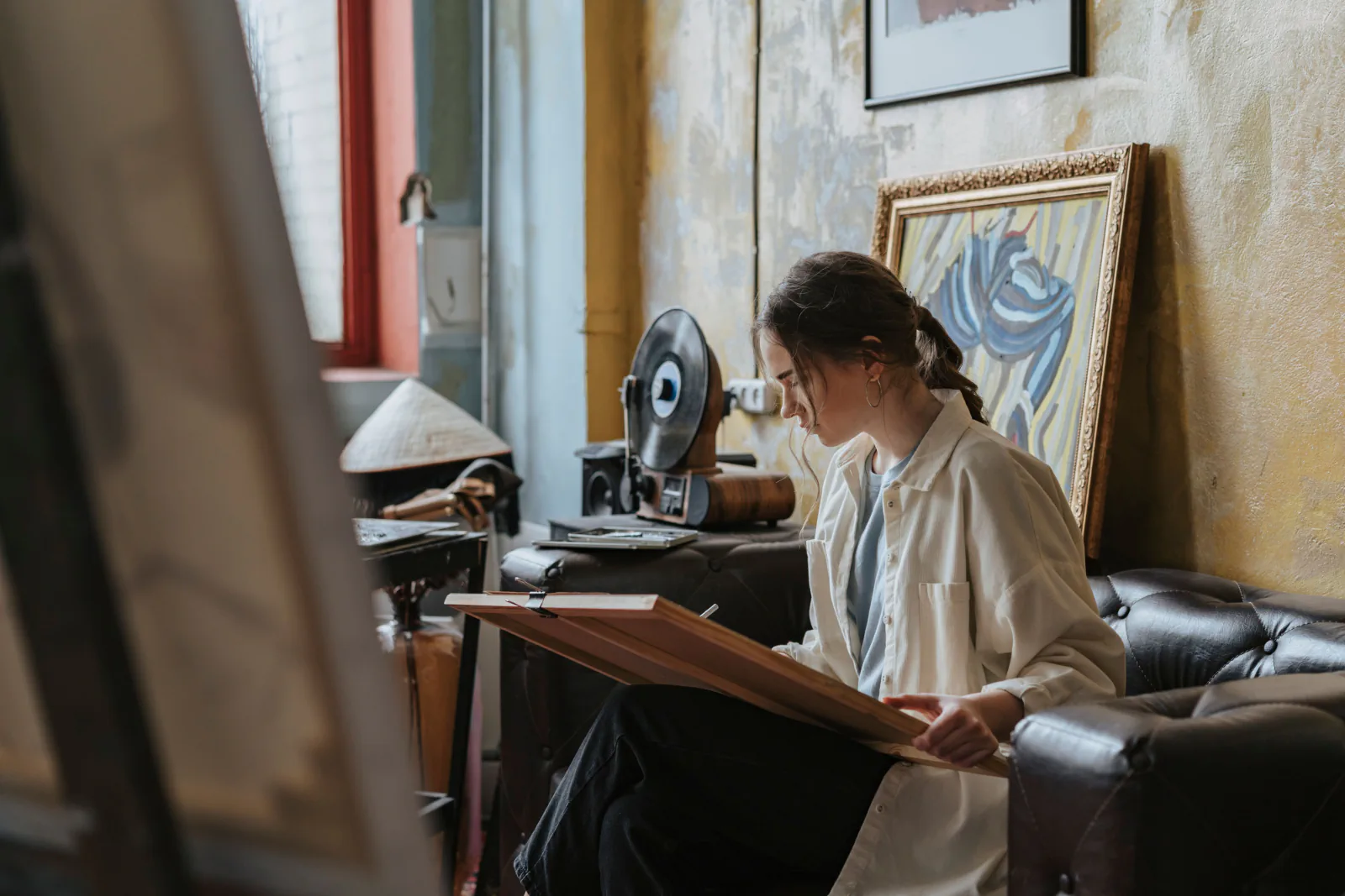 An artist drawing beside an easel in a sunlit studio.