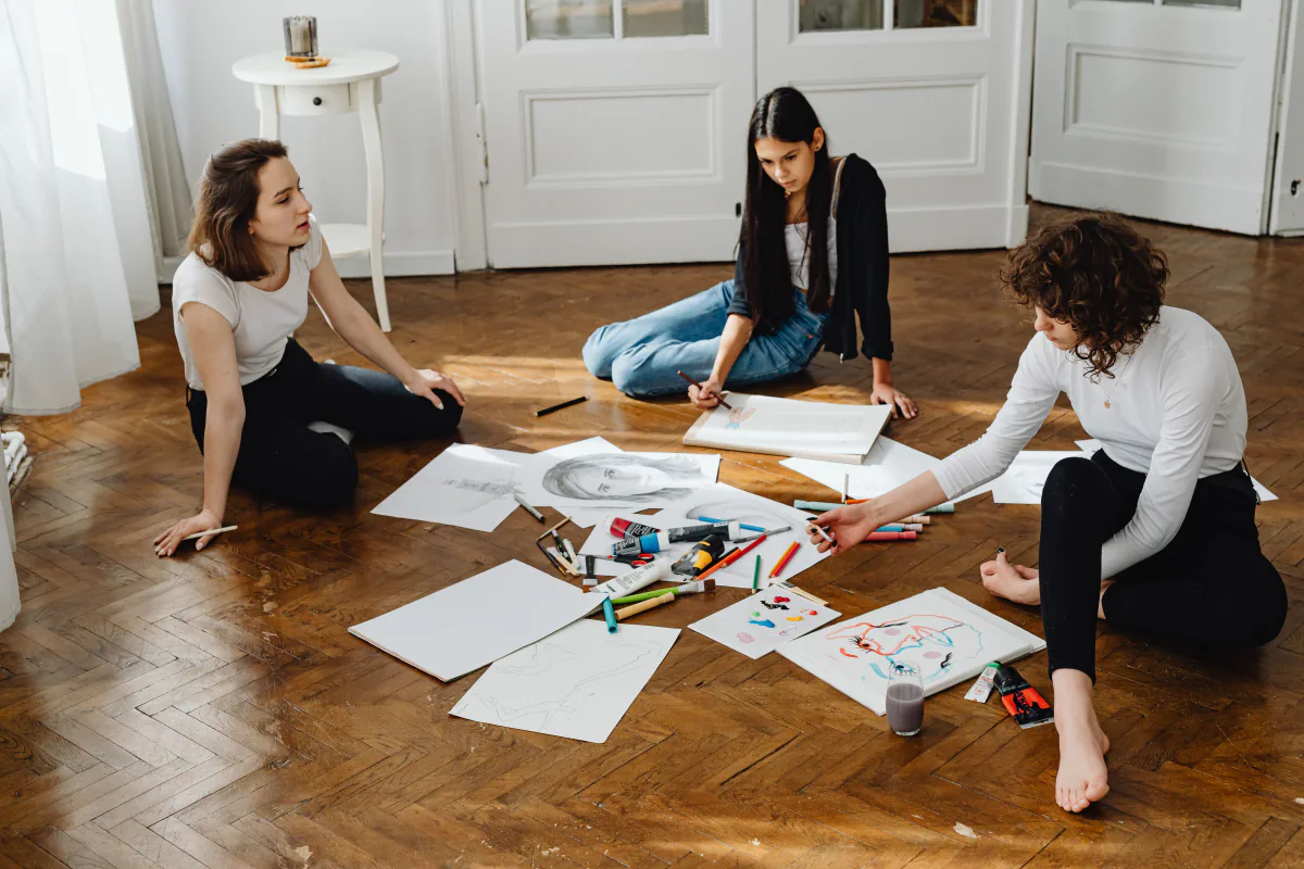 Three artists sitting together and sharing drawings and art materials.